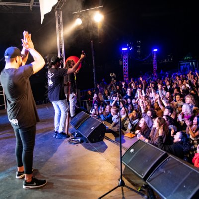 Band playing on stage with crowd in the background.